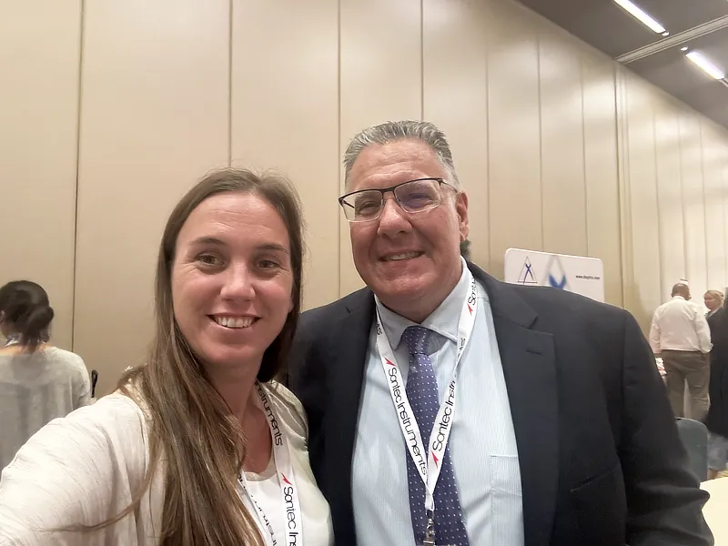 María Simó de IVO posa junto al Dr. John Sapienza en el 5º Congreso de Cirugía Oftalmológica Veterinaria en Chicago, en una zona de exhibición con paneles informativos.