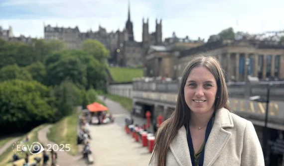 Primer plano de la Dra. María Simó sonriendo al aire libre con vistas panorámicas de Edimburgo al fondo y el logo del ECVO 2025 en la esquina