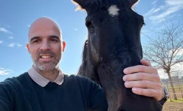 Álvaro Zambrano sonriente acariciando a “IVO Tikal DZ”, una yegua negra con una mancha blanca en la frente, al aire libre y con cielo azul despejado.