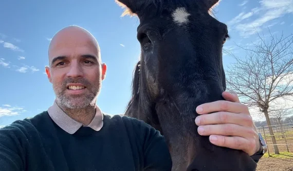 Álvaro Zambrano sonriente acariciando a “IVO Tikal DZ”, una yegua negra con una mancha blanca en la frente, al aire libre y con cielo azul despejado.