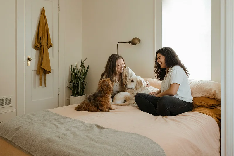 Dos mujeres acarician a sus perros en casa, representando la importancia de los cuidados oculares cotidianos y la revisión atenta del bienestar animal.